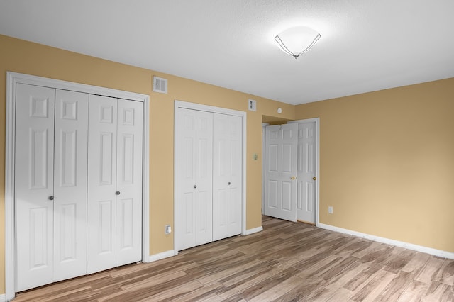 unfurnished bedroom featuring a textured ceiling, two closets, and hardwood / wood-style flooring