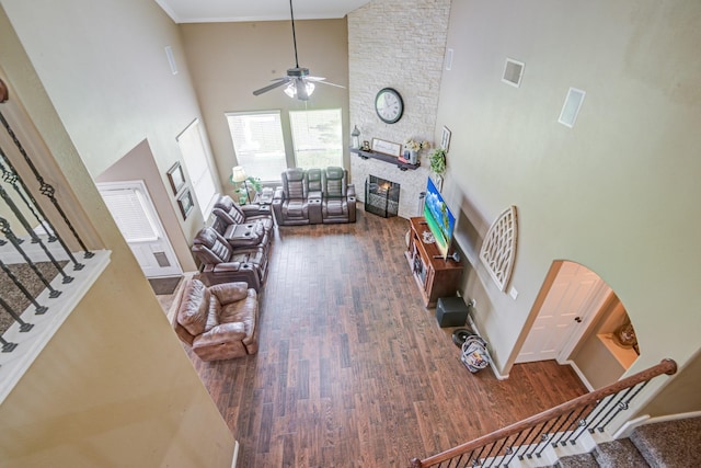 living room with ceiling fan, high vaulted ceiling, dark hardwood / wood-style floors, crown molding, and a fireplace