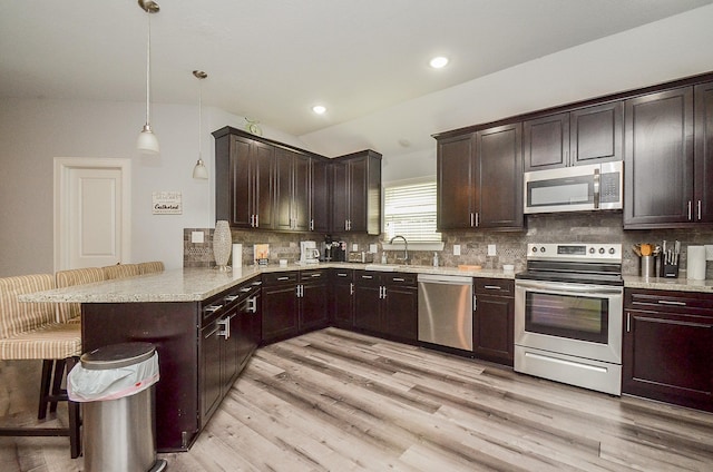 kitchen with kitchen peninsula, a kitchen breakfast bar, stainless steel appliances, decorative light fixtures, and light hardwood / wood-style floors