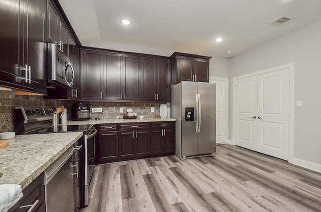 kitchen with light hardwood / wood-style floors, light stone counters, stainless steel appliances, and tasteful backsplash