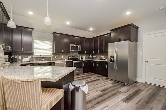 kitchen featuring decorative backsplash, kitchen peninsula, stainless steel appliances, pendant lighting, and light hardwood / wood-style flooring