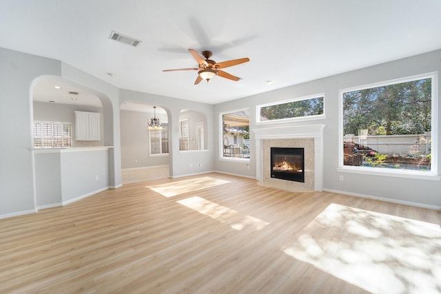 unfurnished living room featuring a tiled fireplace, light hardwood / wood-style floors, and ceiling fan with notable chandelier