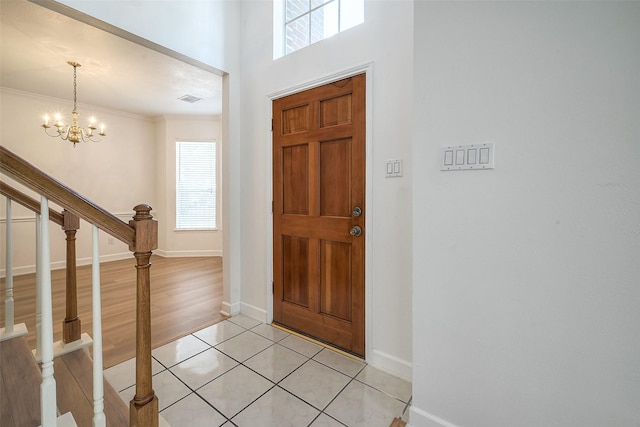 tiled foyer entrance with ornamental molding, a wealth of natural light, and a notable chandelier