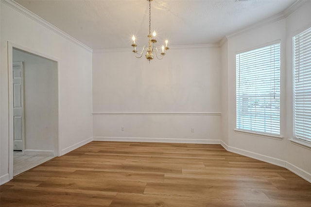 spare room featuring a wealth of natural light, crown molding, light hardwood / wood-style floors, and an inviting chandelier