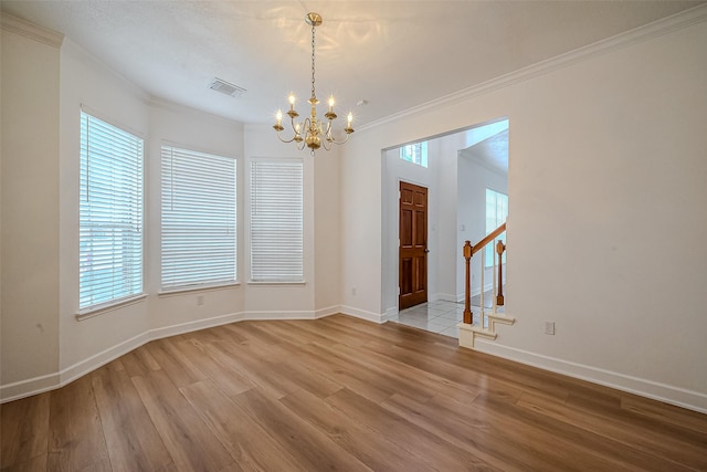 spare room featuring a healthy amount of sunlight, an inviting chandelier, crown molding, and light hardwood / wood-style flooring