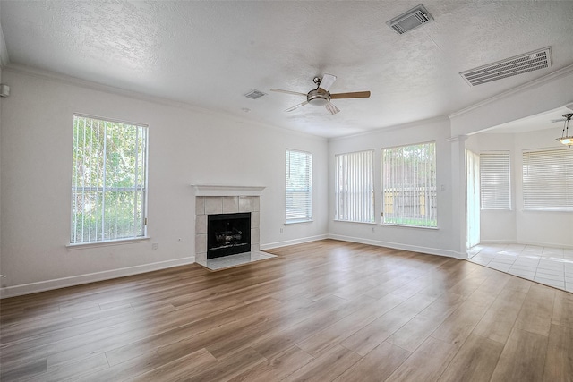 unfurnished living room featuring ceiling fan, crown molding, light hardwood / wood-style floors, a textured ceiling, and a fireplace