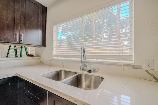 kitchen with light stone counters, sink, and dark brown cabinets