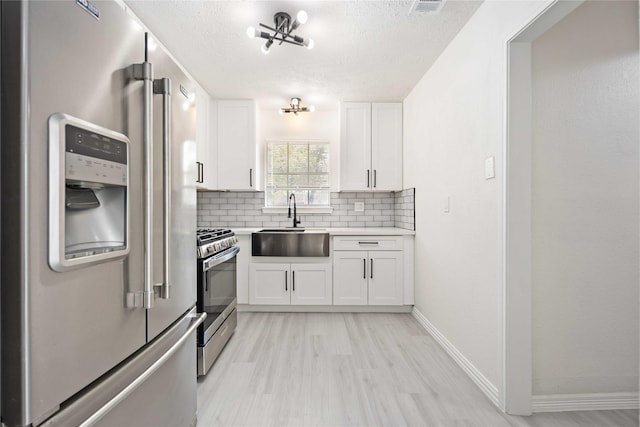 kitchen with white cabinets, sink, decorative backsplash, appliances with stainless steel finishes, and light hardwood / wood-style floors