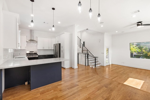 kitchen with sink, light hardwood / wood-style flooring, wall chimney exhaust hood, white cabinetry, and stainless steel appliances