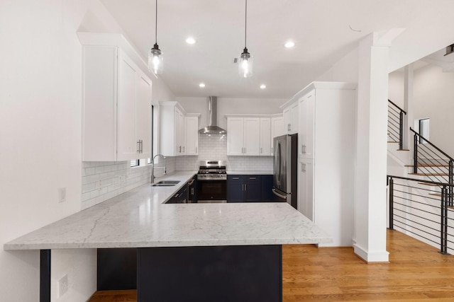 kitchen with white cabinetry, sink, wall chimney range hood, kitchen peninsula, and appliances with stainless steel finishes