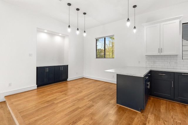 kitchen featuring kitchen peninsula, white cabinets, decorative light fixtures, and light wood-type flooring