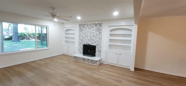 unfurnished living room featuring built in shelves, ceiling fan, a fireplace, and light wood-type flooring