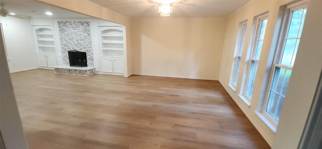 unfurnished living room with built in features, light hardwood / wood-style flooring, and a stone fireplace