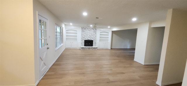 unfurnished living room featuring a stone fireplace, ceiling fan, built in features, and light wood-type flooring