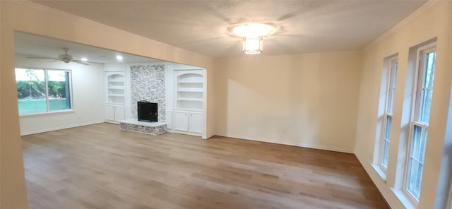 unfurnished living room with built in shelves, ceiling fan, a fireplace, and light hardwood / wood-style floors