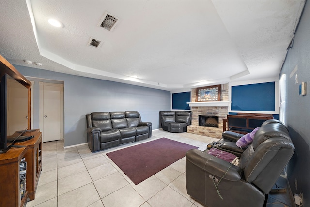 living room with a tray ceiling, a large fireplace, light tile patterned floors, and a textured ceiling