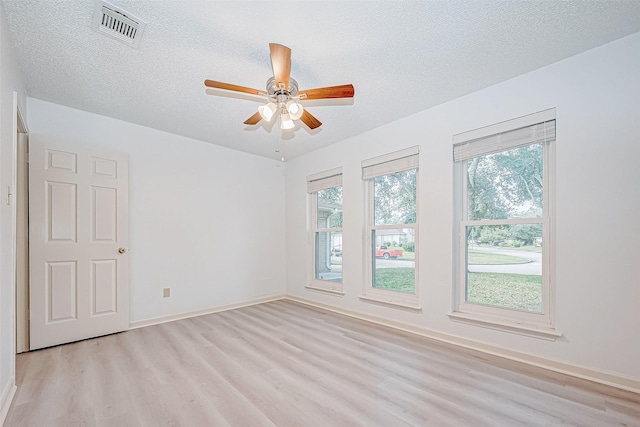 spare room with a textured ceiling, ceiling fan, visible vents, baseboards, and light wood-style floors