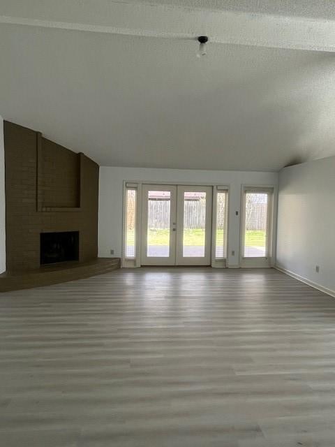 unfurnished living room with a textured ceiling, wood finished floors, vaulted ceiling, french doors, and a brick fireplace