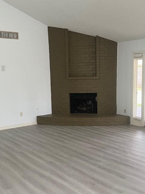 unfurnished living room with lofted ceiling, a fireplace, baseboards, and wood finished floors