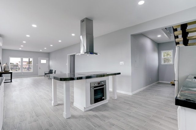 kitchen with island exhaust hood, a kitchen bar, stainless steel oven, white refrigerator, and light hardwood / wood-style flooring