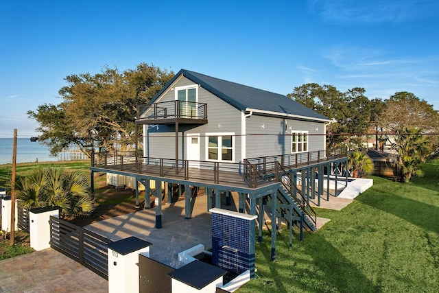 rear view of property with a lawn, a balcony, a deck with water view, and a patio