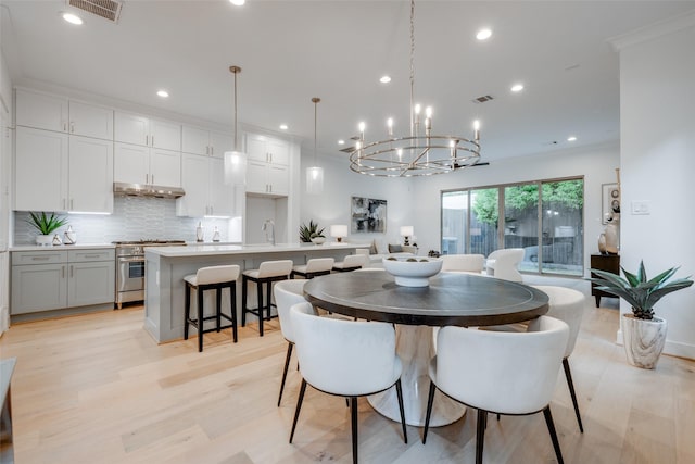 dining space featuring crown molding, light wood-type flooring, sink, and an inviting chandelier