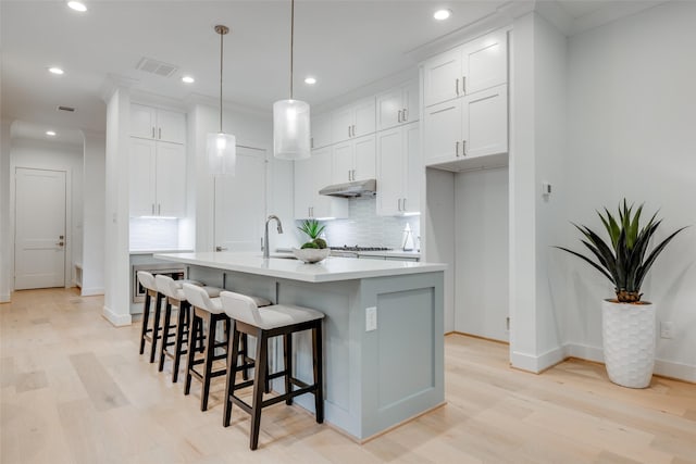 kitchen featuring tasteful backsplash, a kitchen island with sink, white cabinets, light hardwood / wood-style floors, and hanging light fixtures