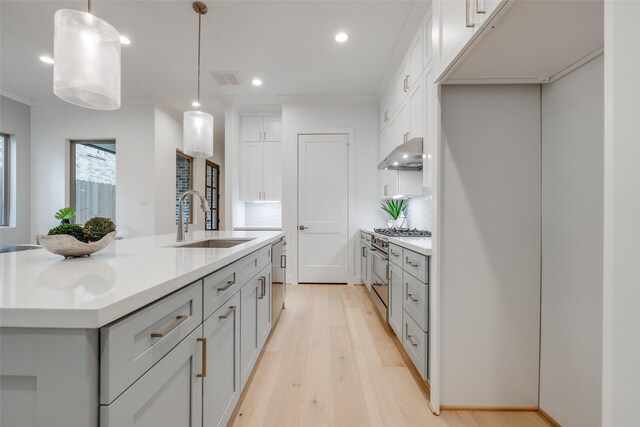 kitchen featuring pendant lighting, sink, light hardwood / wood-style flooring, decorative backsplash, and an island with sink