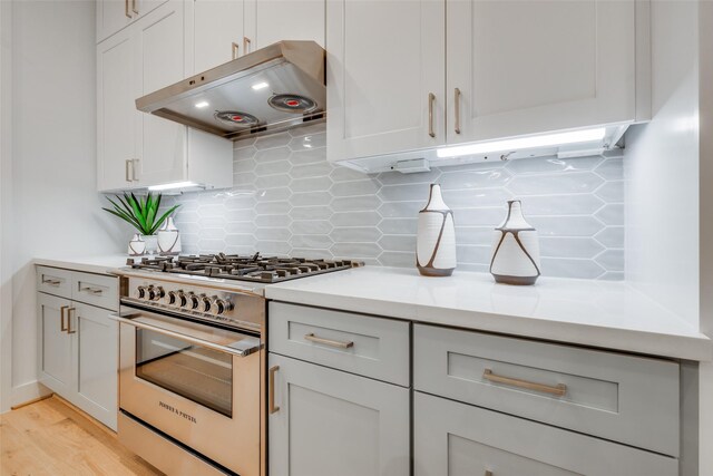 kitchen featuring high end stove, backsplash, and light hardwood / wood-style flooring