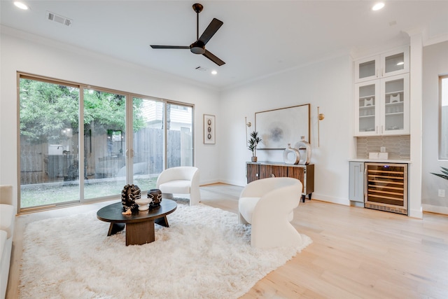 living room featuring ceiling fan, crown molding, light hardwood / wood-style floors, wine cooler, and bar