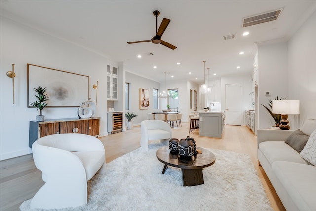 living room with ornamental molding, light hardwood / wood-style floors, ceiling fan, and beverage cooler