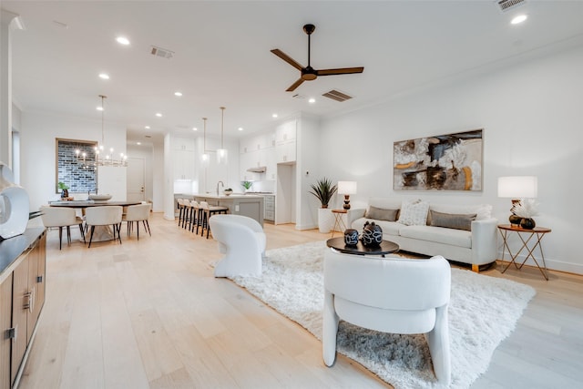 living room featuring sink, light hardwood / wood-style floors, and ceiling fan with notable chandelier