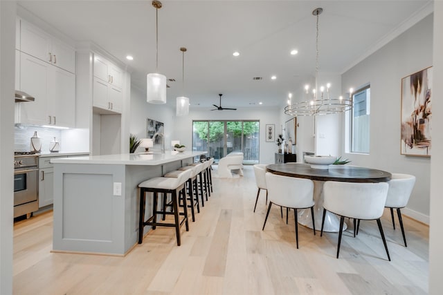 kitchen with ceiling fan with notable chandelier, a kitchen island with sink, stainless steel range oven, white cabinets, and hanging light fixtures