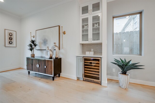 bar featuring crown molding, backsplash, wine cooler, and light hardwood / wood-style flooring