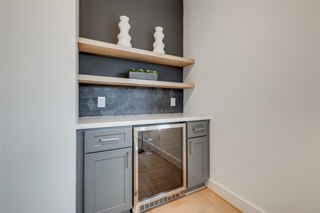 bar featuring backsplash, gray cabinetry, light hardwood / wood-style flooring, and beverage cooler