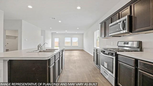 kitchen with sink, stainless steel appliances, a kitchen island with sink, dark brown cabinets, and light wood-type flooring