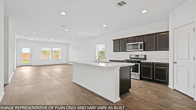 kitchen with a kitchen island with sink, sink, dark brown cabinets, dark hardwood / wood-style flooring, and stainless steel appliances