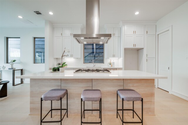 kitchen with island range hood, a spacious island, white cabinets, stainless steel gas stovetop, and a breakfast bar area