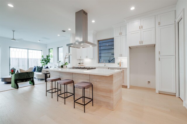 kitchen featuring stainless steel gas stovetop, a breakfast bar area, island range hood, and white cabinets