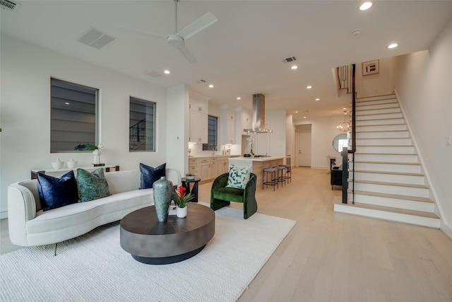 living room with light wood-type flooring, visible vents, a ceiling fan, recessed lighting, and stairway