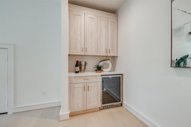 bar featuring baseboards, light wood-type flooring, a bar, wine cooler, and tasteful backsplash