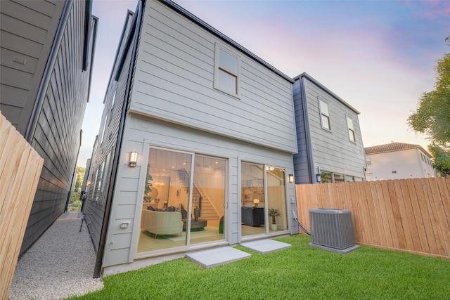 rear view of property featuring a yard, fence, and central AC