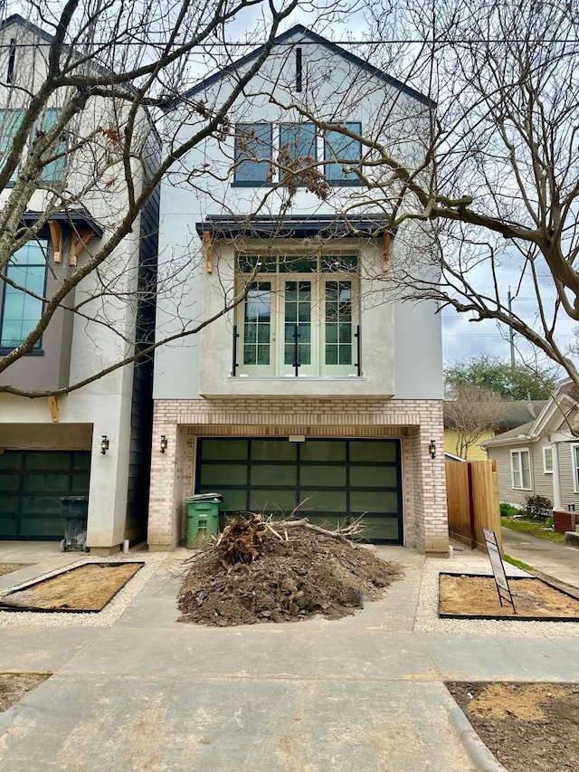 contemporary house with concrete driveway, a garage, brick siding, and stucco siding