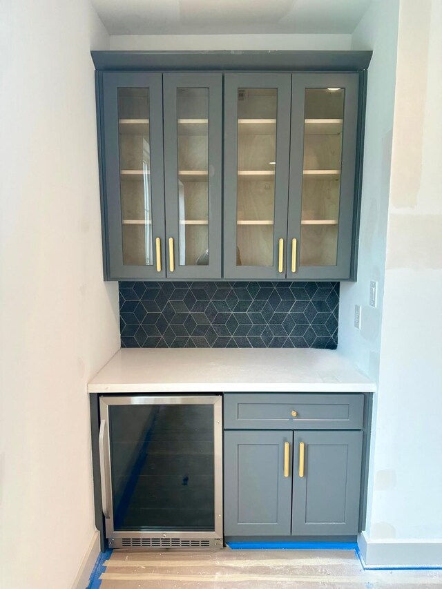 bar with light wood-type flooring, decorative backsplash, wine cooler, and baseboards