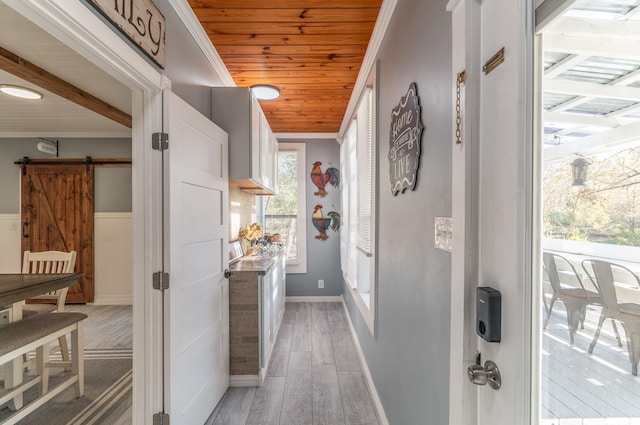 hallway with a barn door, wainscoting, wood ceiling, ornamental molding, and light wood-style floors