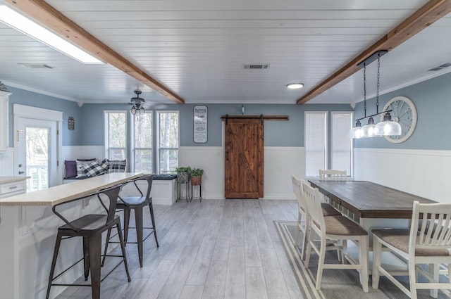 dining room with light wood-type flooring, a wainscoted wall, visible vents, and a barn door