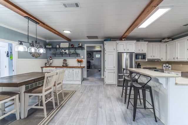 kitchen with visible vents, a wainscoted wall, appliances with stainless steel finishes, white cabinetry, and beam ceiling