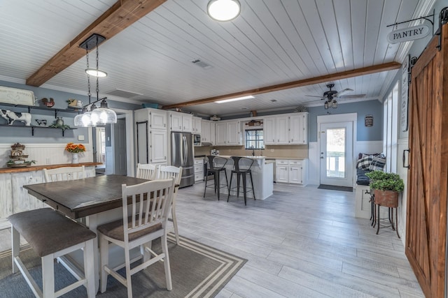 dining space featuring light wood-type flooring, wainscoting, beamed ceiling, and a barn door