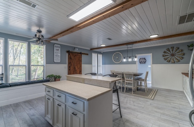 kitchen with beam ceiling, light countertops, a barn door, open floor plan, and wainscoting