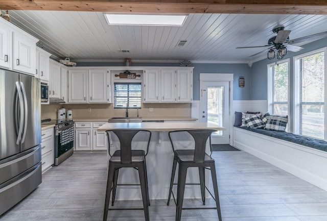 kitchen with white cabinets, a breakfast bar, stainless steel appliances, light countertops, and a sink